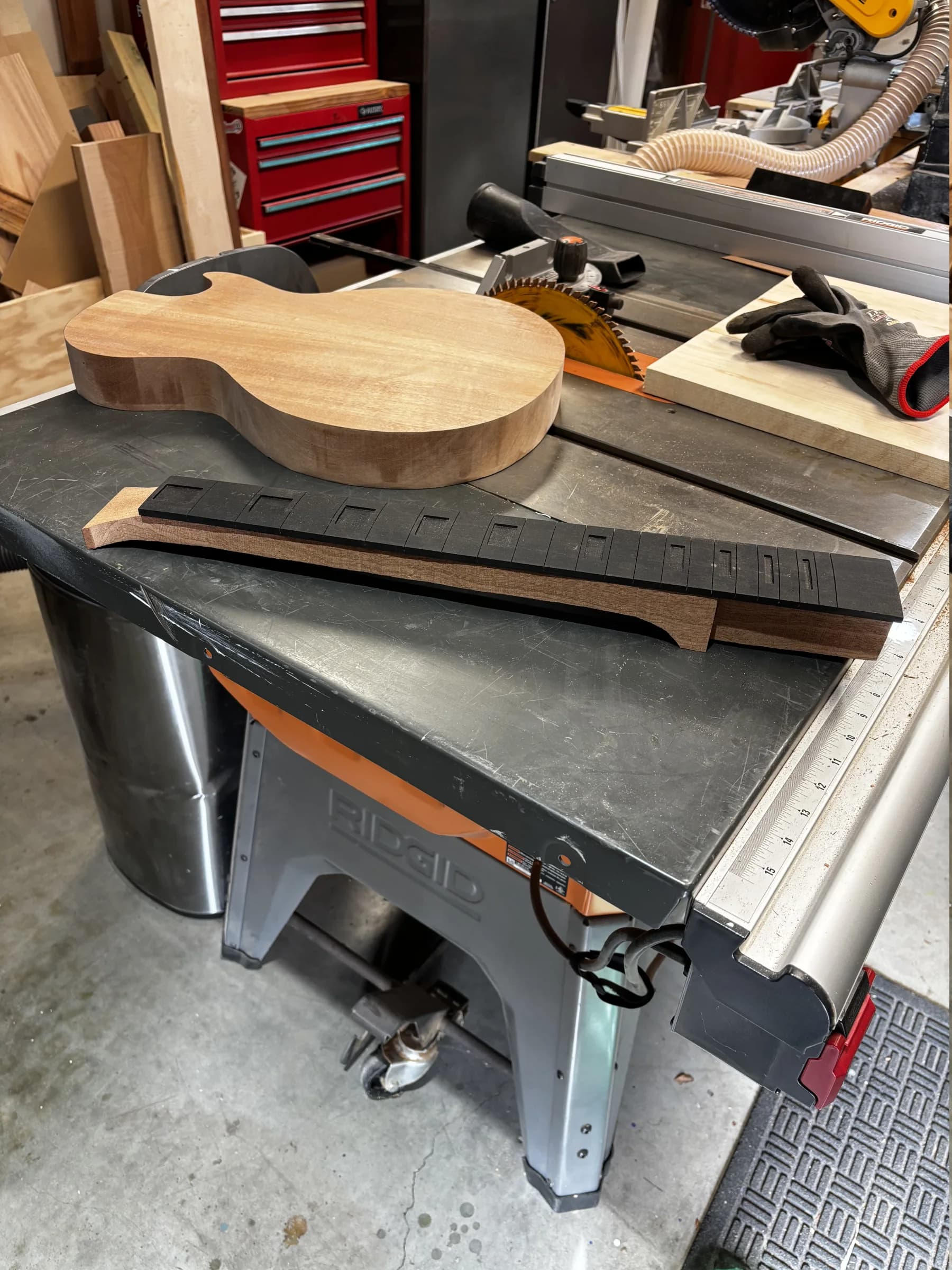 Early-stage guitar body, neck, and fingerboard arranged in a working shop
